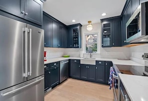 A modern kitchen with dark cabinetry, stainless steel appliances, and a central island. - Classic 3 Bedroom Eastport Cottage with Large Yard and Free Parking (Annapolis)