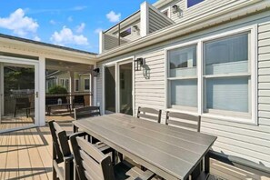 A covered patio with a wooden table and chairs, a sliding glass door leading to an outdoor area, and a white exterior wall with windows. - Classic 3 Bedroom Eastport Cottage with Large Yard and Free Parking (Annapolis)