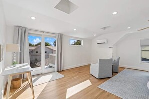 A spacious living area with a large sliding glass door leading to a balcony, a white desk with a lamp, and a grey sofa. - Classic 3 Bedroom Eastport Cottage with Large Yard and Free Parking (Annapolis)