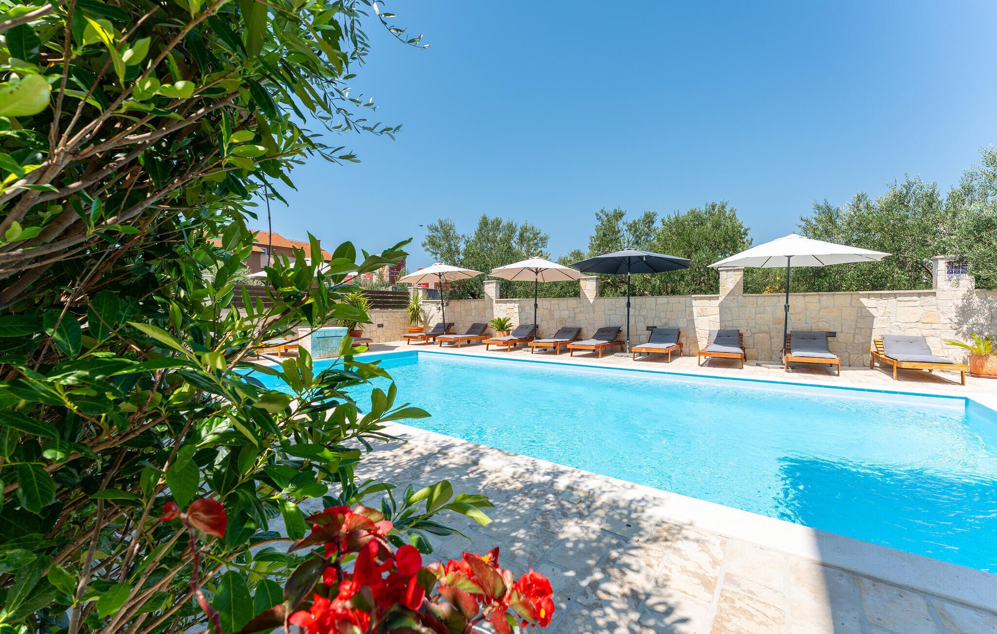 Un espace aménagé au bord de la piscine, avec des chaises longues et des parasols, entouré de verdure et délimité par un mur en pierre.