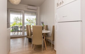 A modern kitchen with a refrigerator, dining table, chairs, and a view of the outdoors through large windows. - Stunning apartment in Turanj with WiFi (Turanj)