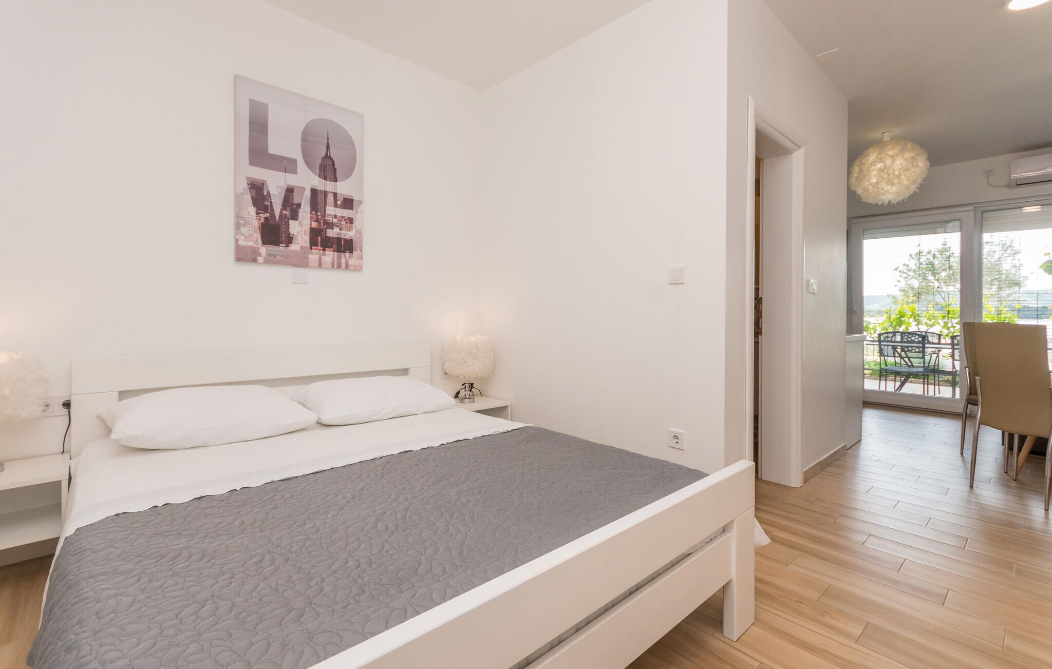 A modern bedroom with a bed, bedside lamps, a cityscape poster, and a view of the outdoors.