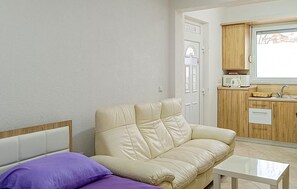 A living room with a beige sofa, a small white table, and a purple pillow. There is a kitchen area with wooden cabinets and a microwave. - Cozy apartment in Vir with WiFi (Vir)