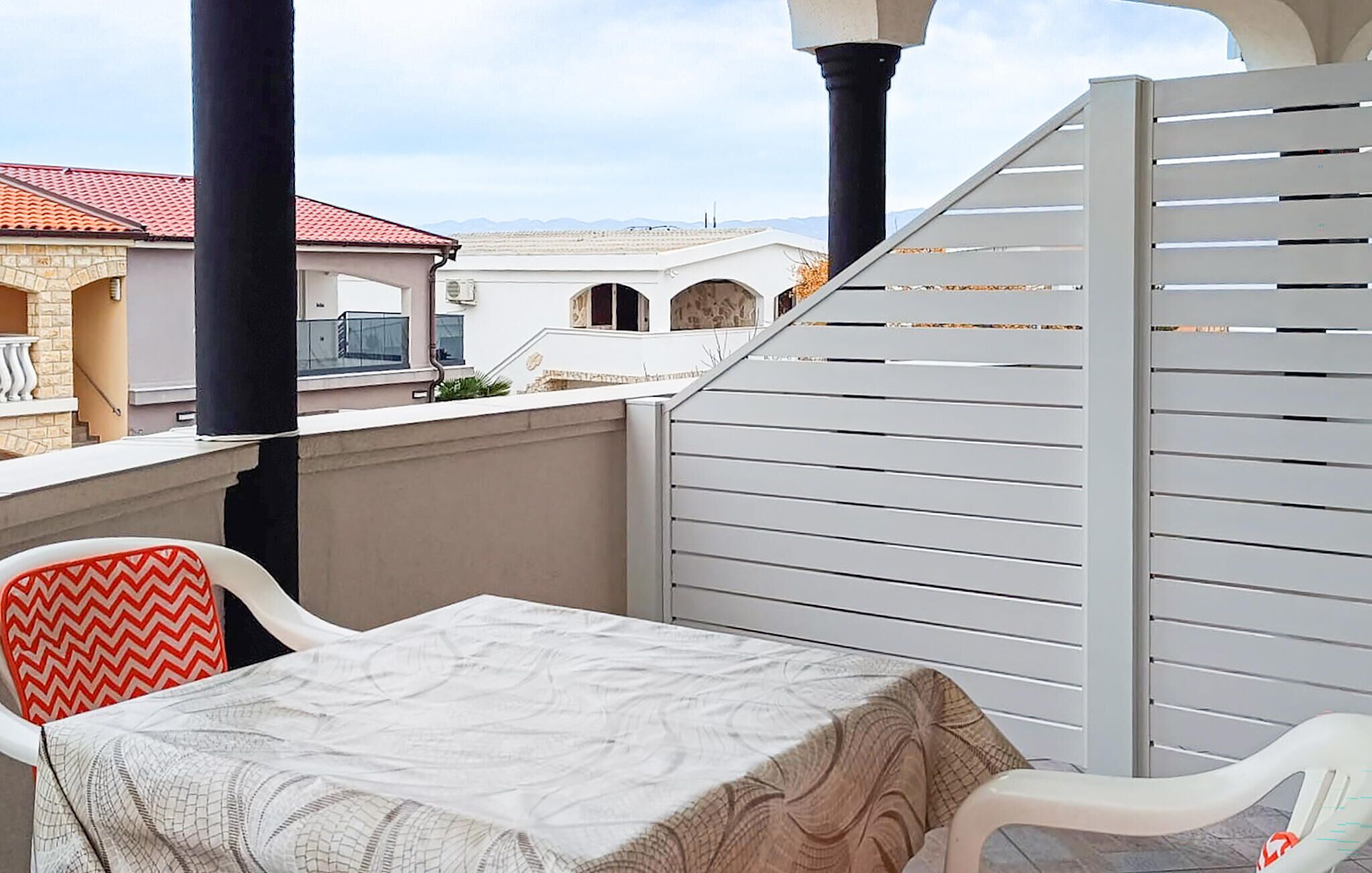 Un balcon avec une table et des chaises, une clôture blanche et des bâtiments en arrière-plan.