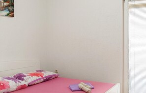 Ein Schlafzimmer mit einem Bett, einem Kissen und einem zusammengerollten Handtuch auf einer rosafarbenen Matratze.