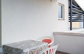 Ein Balkon mit weißem Stuhl und Tisch, einem Fenster und einem Metallgeländer.