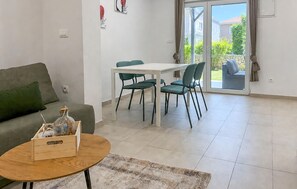 Ein Wohnzimmer mit einer Couch, einem Esstisch mit Stühlen, einem kleinen Holztisch mit einer Flasche und einem gemusterten Teppich.