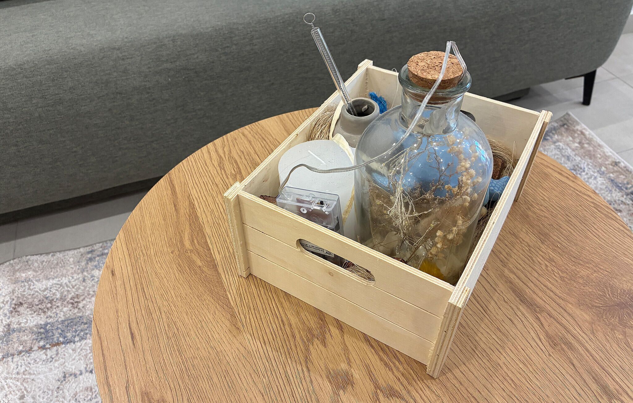 Una caja de madera con una botella de vidrio y tapón de corcho, un recipiente metálico y una bolsa de plástico.