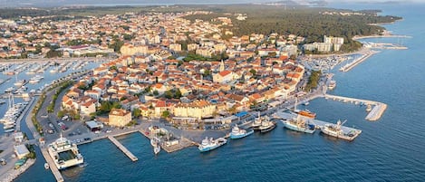 An aerial view of a coastal town with a marina, dense housing, and a clear view of the sea.