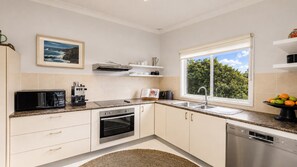 A modern kitchen with a built-in oven, microwave, and dishwasher. There's a window with a view of greenery outside. - Sunny Bayside Cottage - Walk to bay and village (HARDYS BAY)