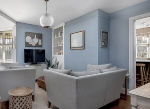 A living room with a sectional sofa, a television, and a decorative pendant light. - East Lodge (Peterborough)