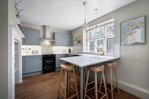 A modern kitchen with a central island, bar stools, and a window with blinds. - East Lodge (Peterborough)