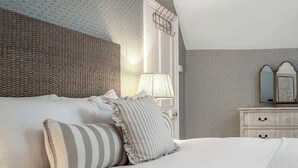 A neatly made bed with pillows and a striped pillow, a bedside lamp, a dresser with drawers, and patterned wallpaper. - East Lodge (Peterborough)