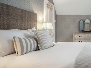 A neatly made bed with pillows and a striped pillow, a bedside lamp, a dresser with drawers, and patterned wallpaper. - East Lodge (Peterborough)