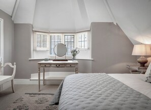 Une chambre à coucher avec un lit, une commode avec un miroir, un banc et une fenêtre avec des stores.