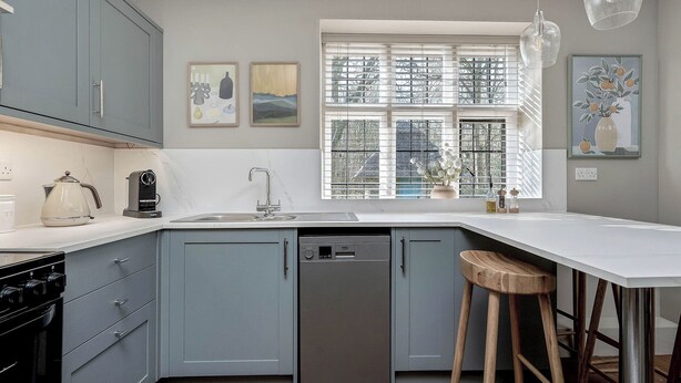 A kitchen with grey cabinets, a dishwasher, a sink, and a window with blinds. - East Lodge (Peterborough)