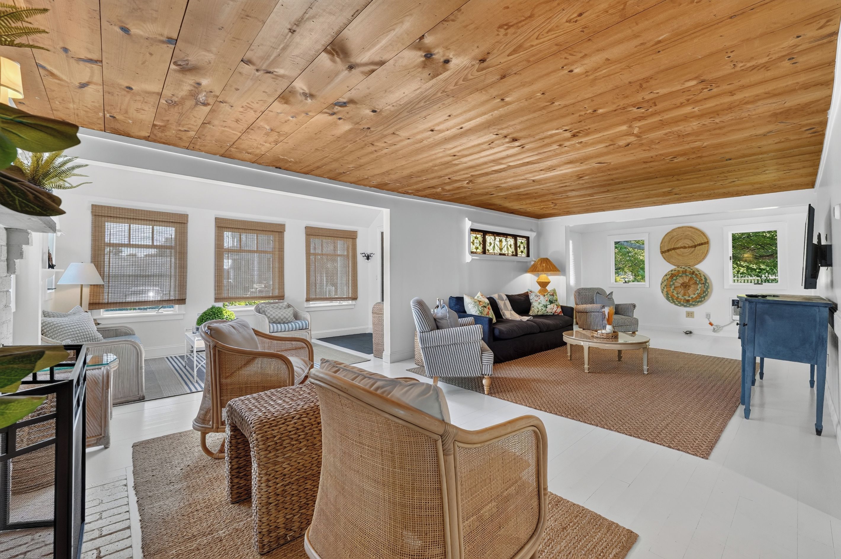 A spacious living room with a high wooden ceiling, wicker furniture, a black sofa, and a blue table.