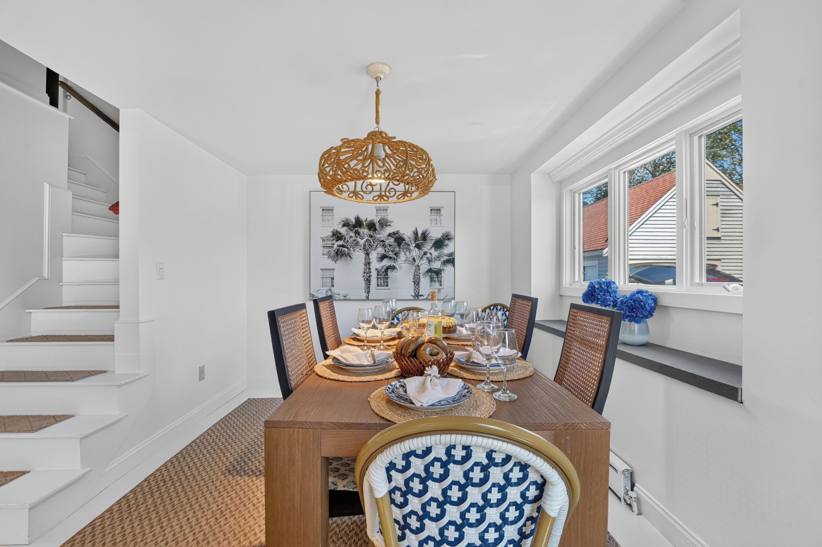 A dining room with a wooden table set for six, a chandelier, and a window with blue flowers.