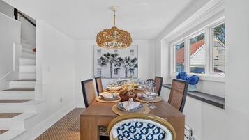 A dining room with a wooden table set for six, a chandelier, and a window with blue flowers.