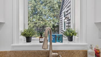 Un lavello da cucina con un rubinetto moderno, due piante in vaso e una finestra che si affaccia su alberi e un edificio.