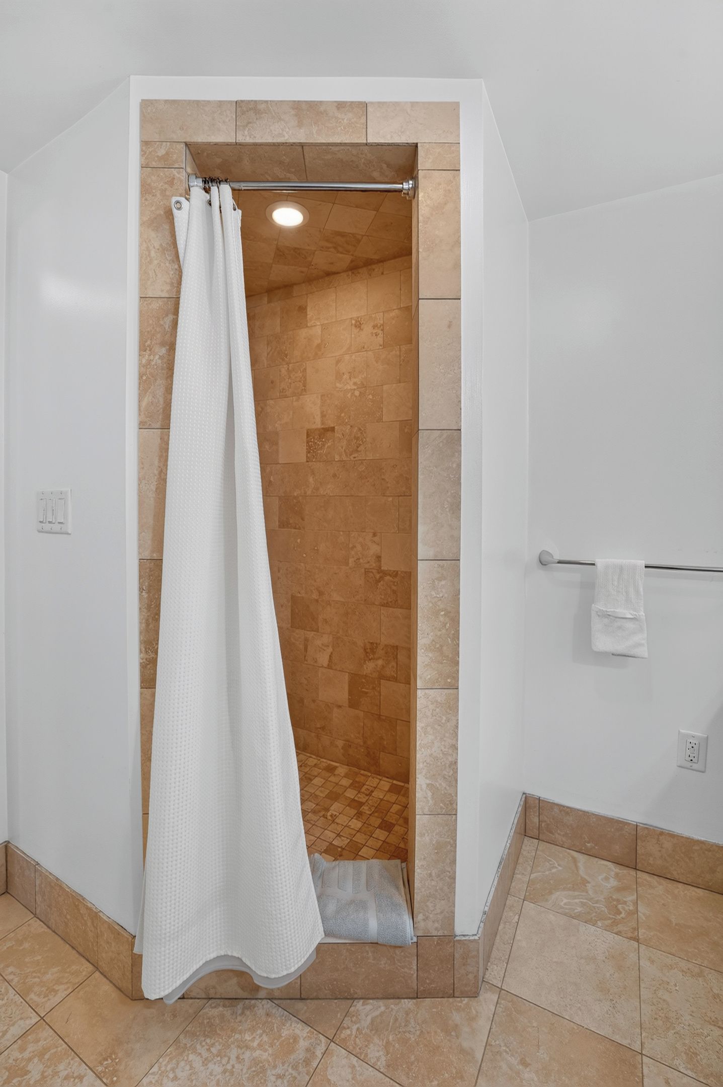 Un espace douche avec un rideau de douche blanc, un porte-serviettes avec une serviette, et un sol carrelé.