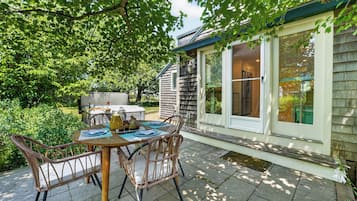 Un patio con tavolo e sedie, un barbecue e una casa con una finestra che si affaccia sul giardino.