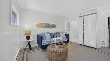 A modern living room with a blue sofa, a round woven coffee table, and a wall-mounted decorative piece.