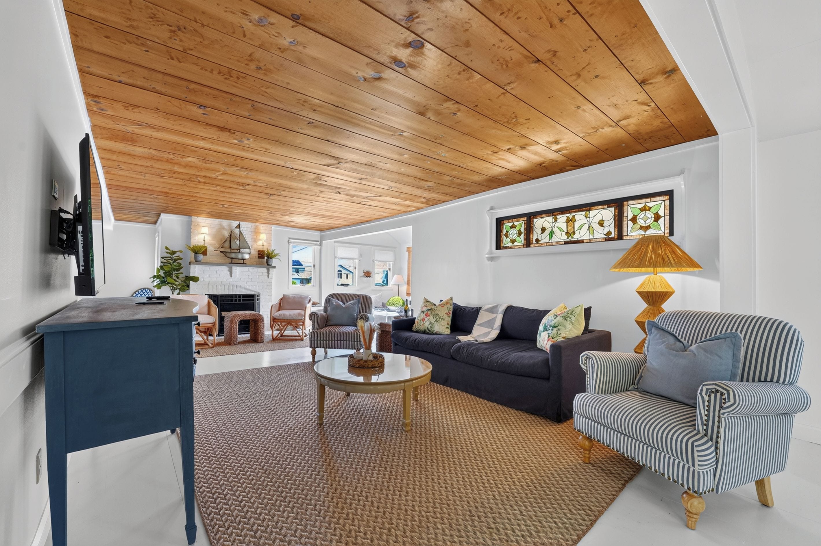 A spacious living room with a high wooden ceiling, a fireplace, and a large window.