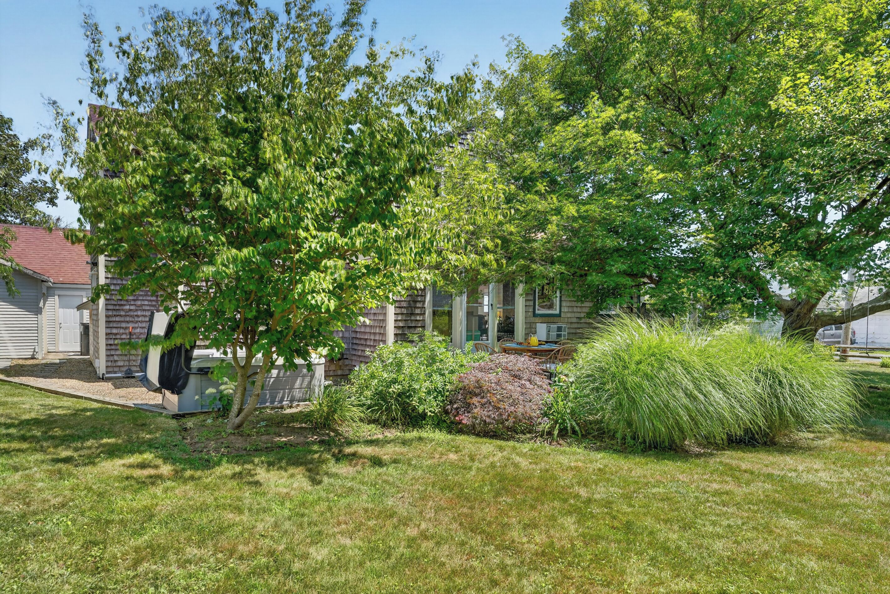 A residential property with a well-maintained lawn, a variety of shrubs, and a tree providing shade.