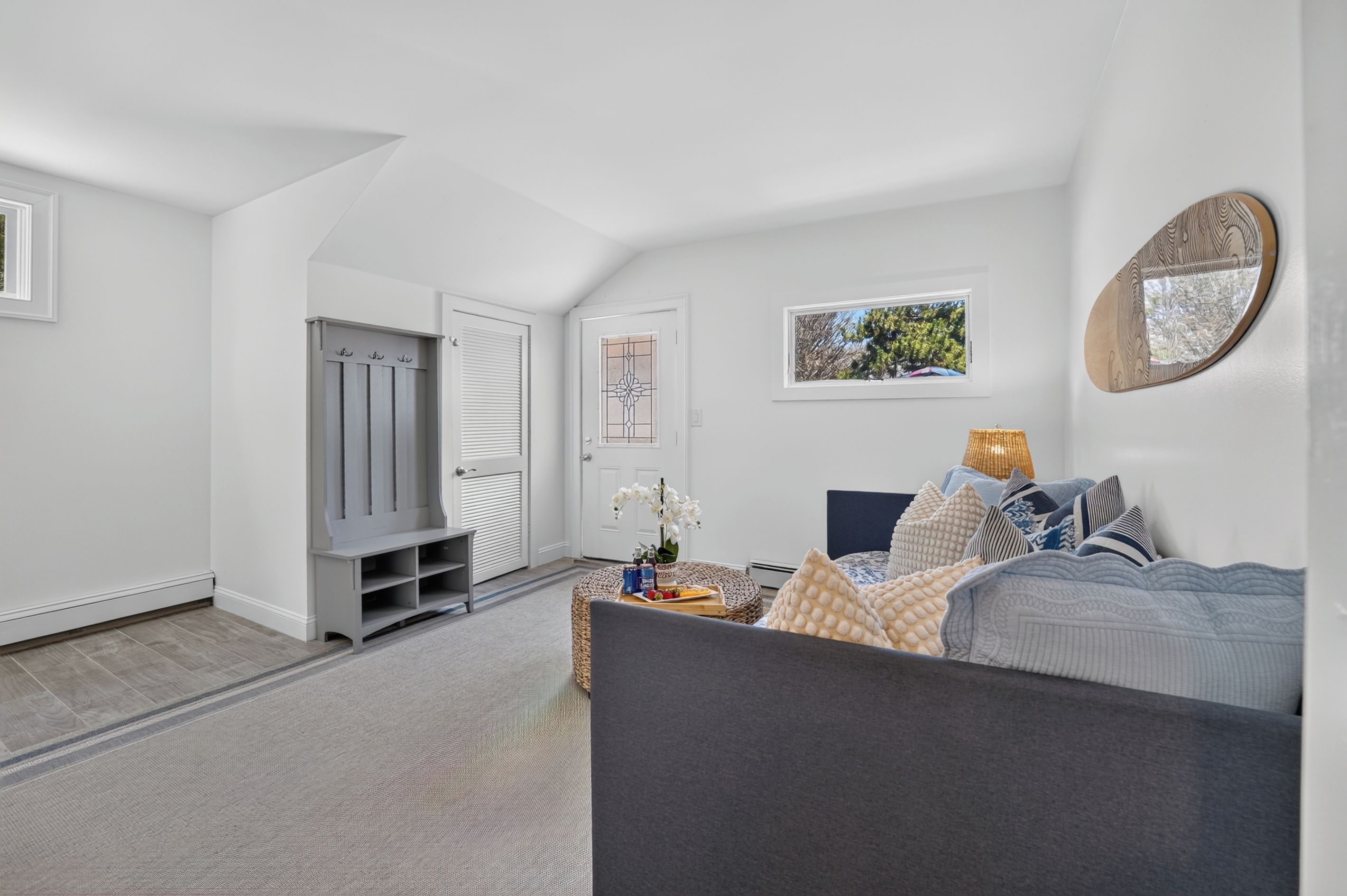Ein modernes Wohnzimmer mit einem grauen Sofa, einem Couchtisch mit Snacks, einem Fernseher und einem Fenster mit Blick auf Bäume.