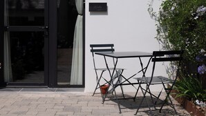 Un edificio moderno con un ingresso con porta in vetro, un piccolo tavolo all'aperto con sedie e una pianta in vaso accanto all'ingresso.