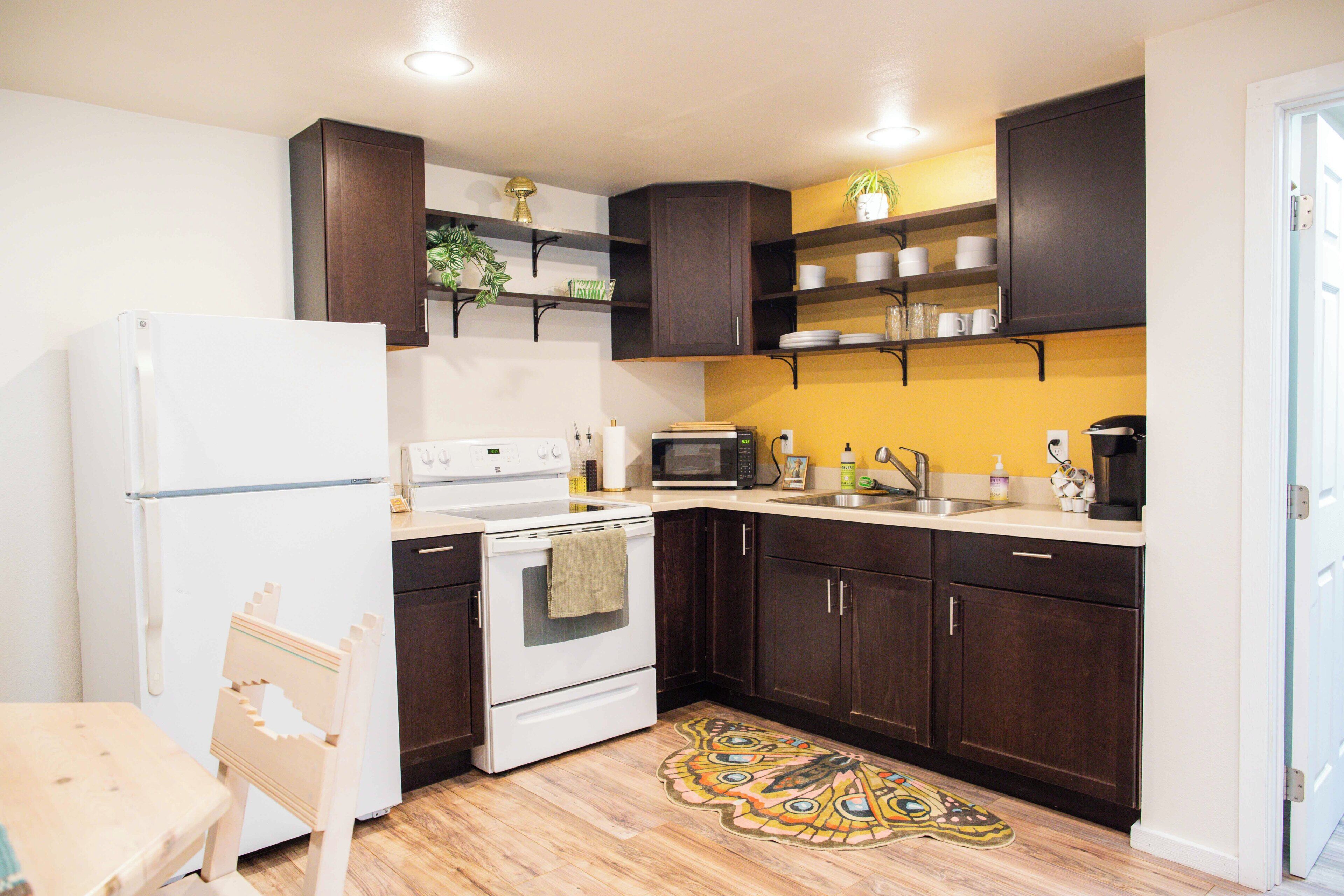 A compact kitchen with dark cabinetry, a white refrigerator, a microwave, and a stove.