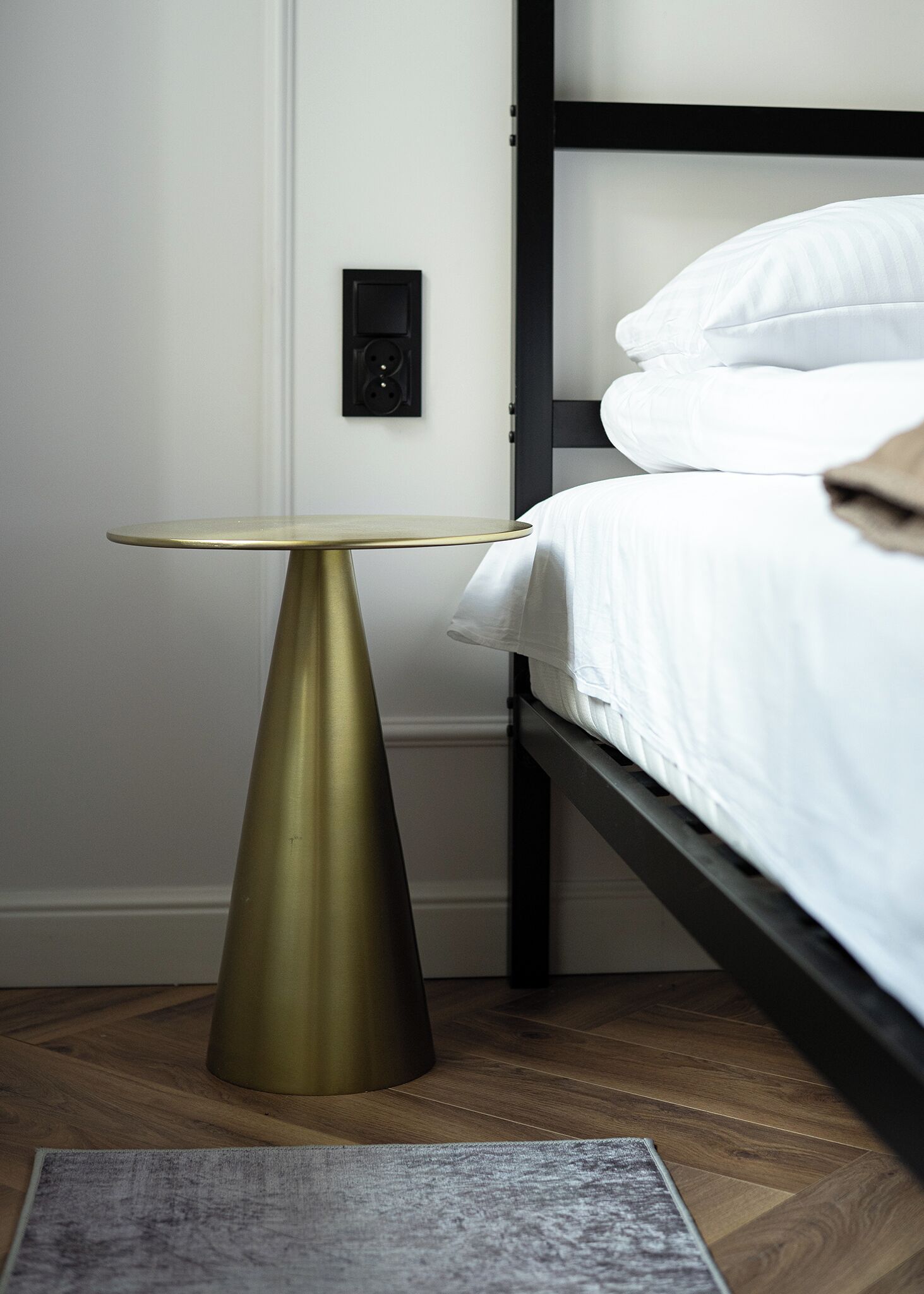 A bed with white bedding, a black headboard, and a bedside table with a gold-colored base.