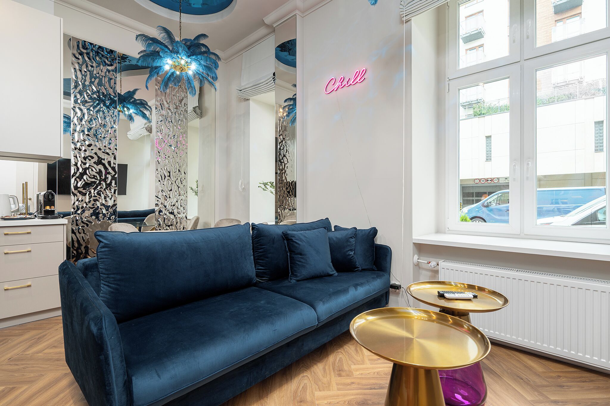 A modern living room with a blue sofa, two gold side tables, and a neon sign on the wall.