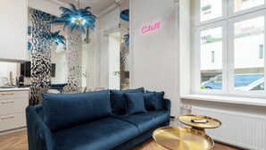 A modern living room with a blue sofa, two gold side tables, and a neon sign on the wall. - RentPlanet - Apartamenty Kilińskiego (Łódź)