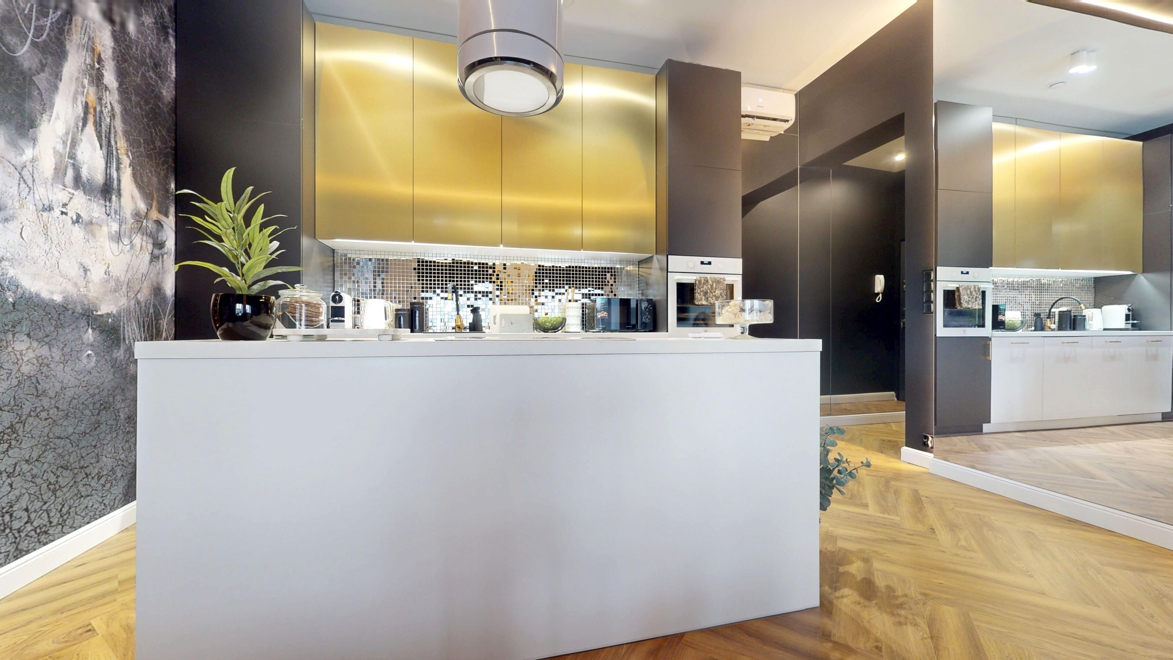 A modern kitchen with a central island, a backsplash with mosaic tiles, and a potted plant.