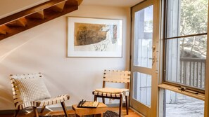 A room with a wooden ceiling, a large window, two chairs, a chessboard, and a framed abstract painting. - Coastal Wilderness Retreat (HARDYS BAY)