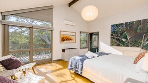 A bedroom with a large bed, a dresser, a chair, and a window overlooking a balcony. - Coastal Wilderness Retreat (HARDYS BAY)