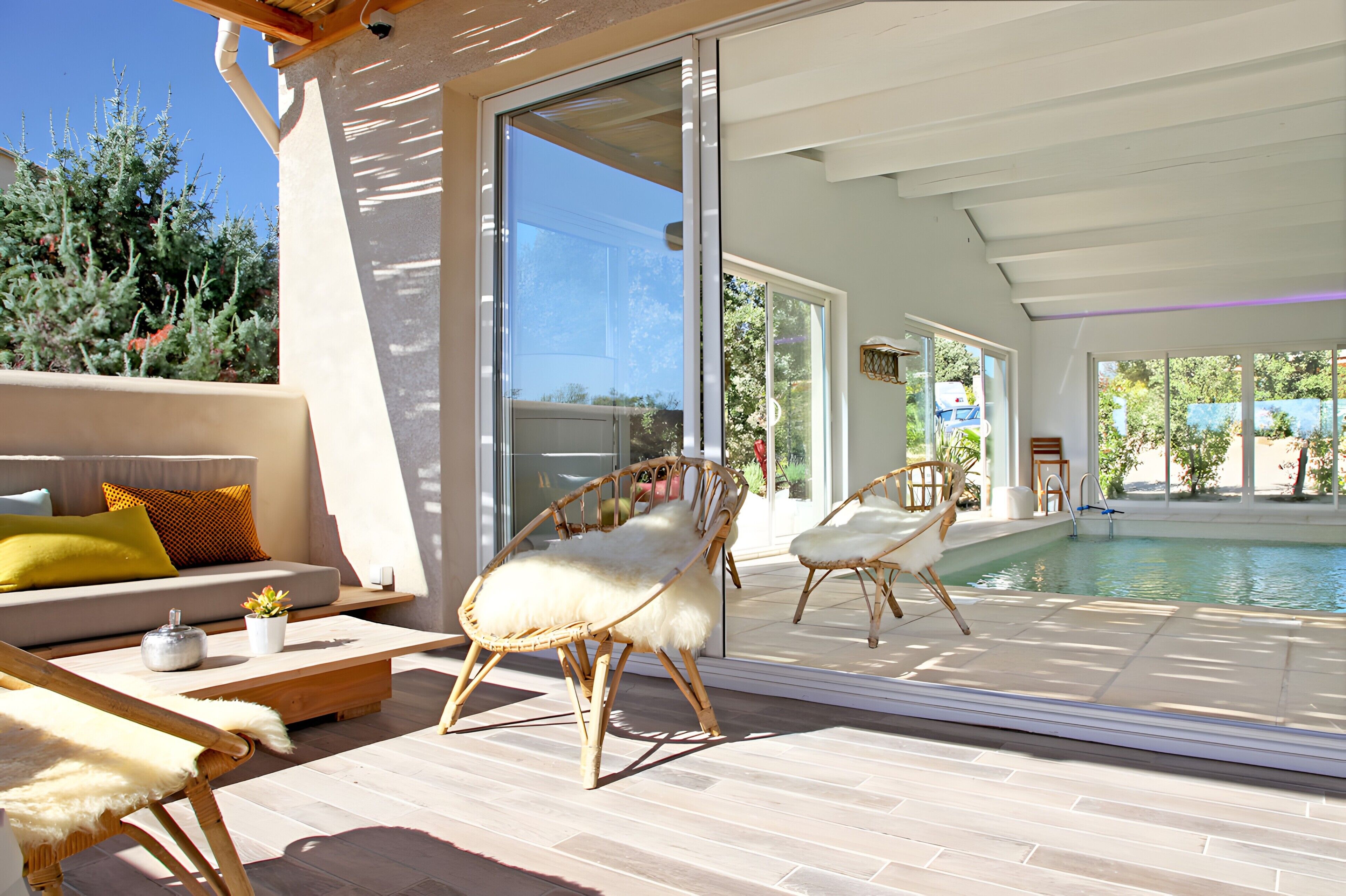 Un espace de vie extérieur moderne avec une piscine, des meubles en osier et un canapé agrémenté de coussins.