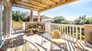Une terrasse extérieure couverte, aménagée avec un canapé, des fauteuils et un coin repas.