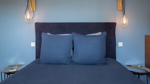Un lit avec une tête de lit sombre et deux oreillers, flanqué de deux tables de chevet avec des lampes.