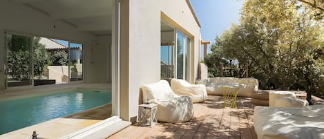 A modern outdoor pool area with a wooden deck, covered seating, and a glass-enclosed patio.