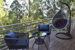 A deck with a hanging chair, two chairs, and a small table. - Pacific Inn Prakrti the nature Lansdowne (Lansdowne)