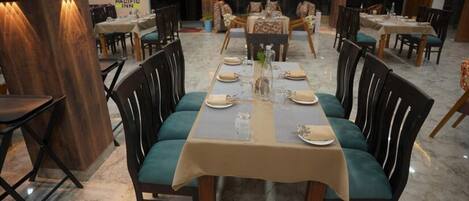 Un restaurante con una larga mesa de comedor dispuesta para cuatro personas, rodeada de sillas con cojines verdes.