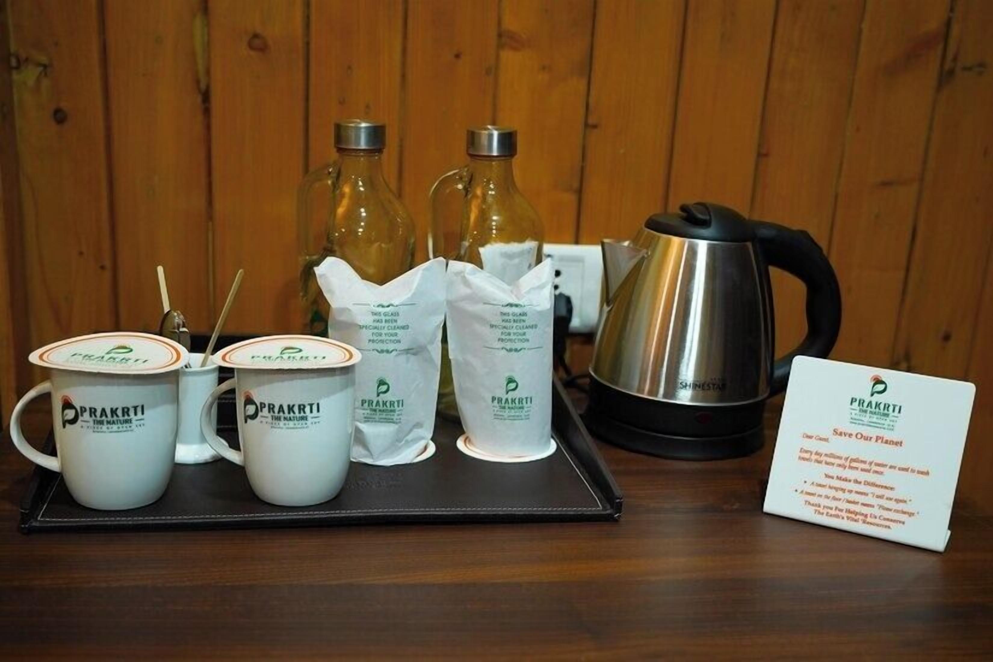 A tray with coffee cups, sugar packets, a kettle, and a sign with the logo 'PRAKRTI'.