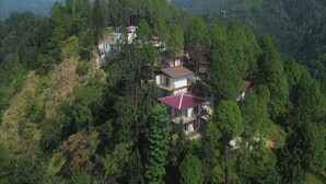 A cluster of houses nestled among dense forest, with multiple levels and varying roof colors. - Pacific Inn Prakrti the nature Lansdowne (Lansdowne)