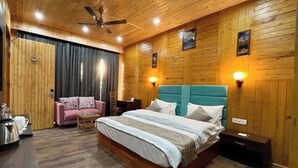 A bedroom with a wooden ceiling, a bed with a teal headboard, a pink sofa, and a small table. - Pacific Inn Prakrti the nature Lansdowne (Lansdowne)