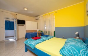 Ein Zimmer mit Bett, Tisch, Stuhl, Fernseher und einem fensterbepflanzten Fenster.