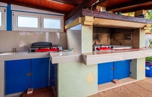 Eine Außenküche mit Gasherd, Grill und blauen Schränken.