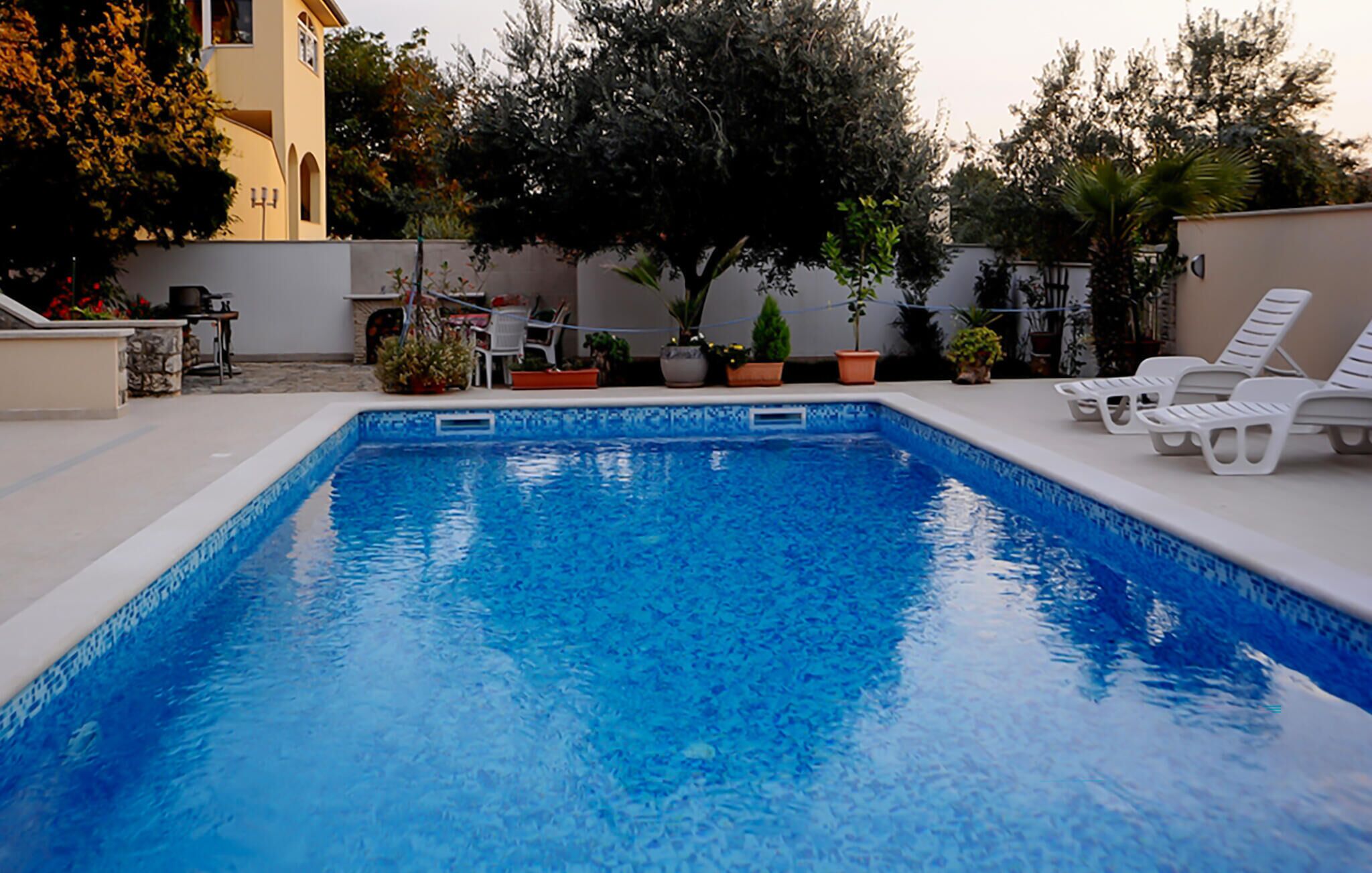 Una piscina rettangolare con acqua cristallina, circondata da poltroncine bianche e piante in vaso.